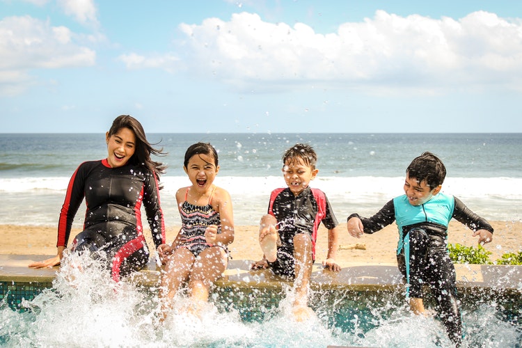 A mother with her three children, splashing in a swimming pool next to a beach.